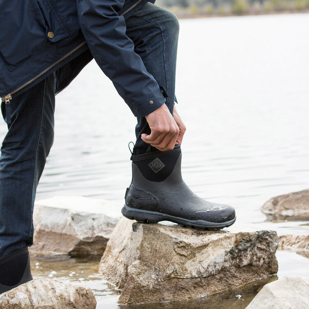 Person wearing black rain boots on a rocky shoreline