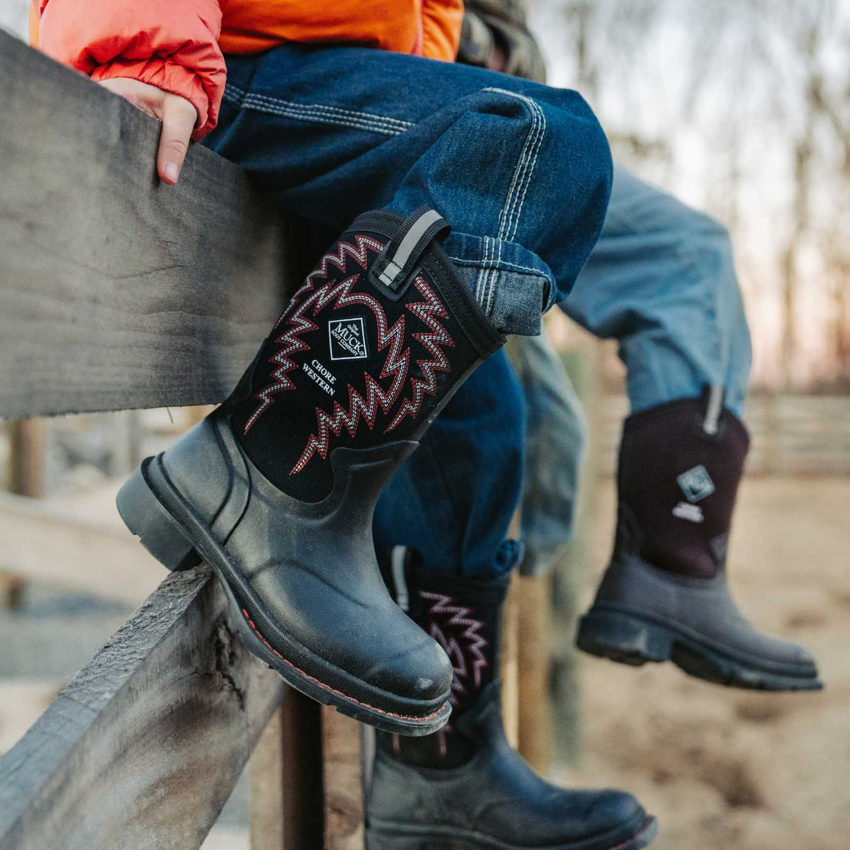 Person wearing black boots with red patterns, sitting on a wooden fence outdoors.